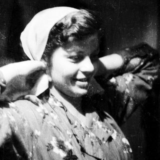 Vintage black-and-white portrait of smiling woman in headscarf.