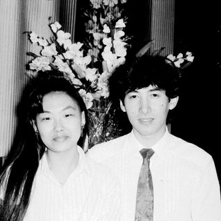 Two people posing formally indoors with floral arrangement.