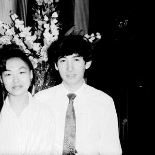 Two people posing formally indoors with floral arrangement.