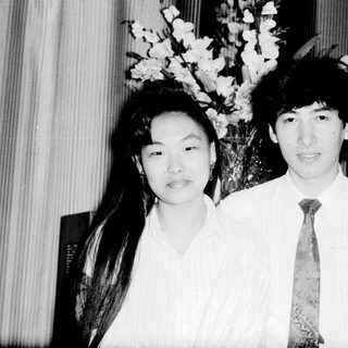 Two people posing formally indoors with floral arrangement.