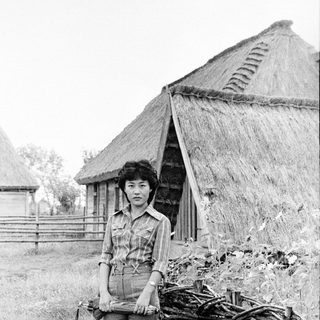 Woman standing outdoors near traditional thatched huts.