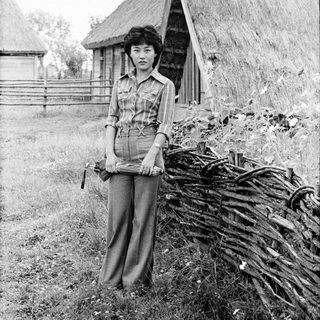 Woman standing outdoors near traditional thatched huts.