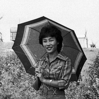 Woman holding striped umbrella outdoors near windmills.