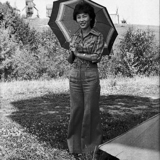 Woman holding striped umbrella outdoors near windmills.