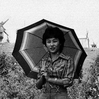 Woman holding striped umbrella outdoors near windmills.