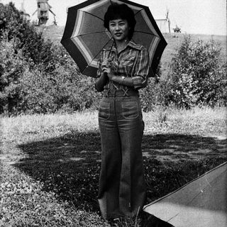 Woman holding striped umbrella outdoors near windmills.