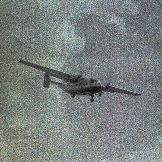 Small aircraft flying through cloudy sky.