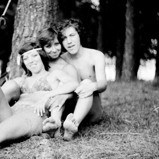 Three shirtless children posing together outdoors in a forest.