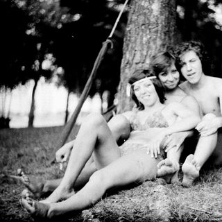 Three shirtless children posing together outdoors in a forest.