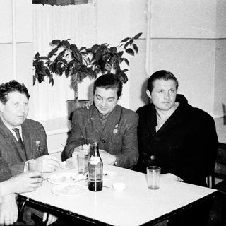 Four men in formal attire dining indoors, mid-20th century.