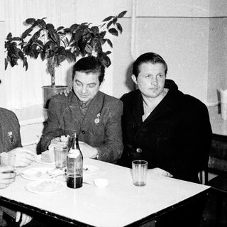 Four men in formal attire dining indoors, mid-20th century.