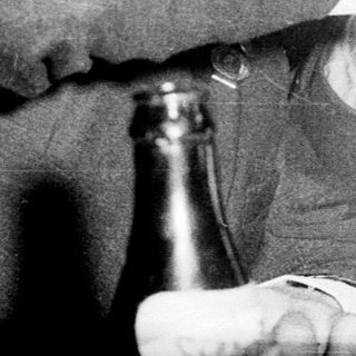 Two men sharing a drink playfully indoors.