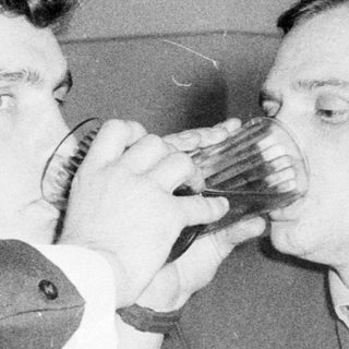Two men sharing a drink playfully indoors.