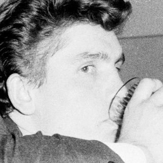 Two men sharing a drink playfully indoors.