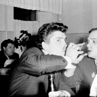 Two men sharing a drink playfully indoors.