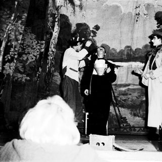 Theatrical performance scene with actors in period costumes.
