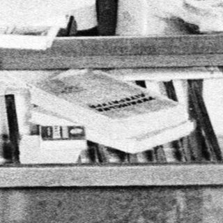 Shirtless man shaving in a cluttered room.