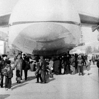 Large airship with crowd of people underneath.