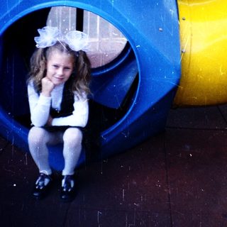 Young girl sitting inside colorful playground tunnel.