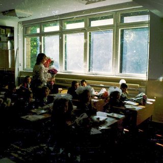 Classroom with students writing at desks, teacher standing.
