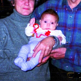 Family portrait with grandparents holding baby indoors.