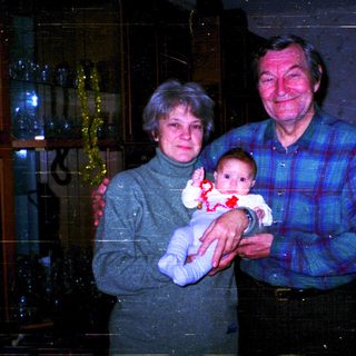 Family portrait with grandparents holding baby indoors.