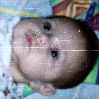 Baby wearing colorful pajamas lying on patterned blanket.