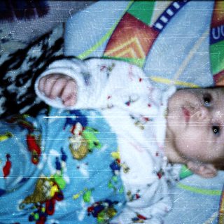 Baby wearing colorful pajamas lying on patterned blanket.