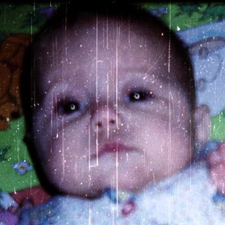 Baby wearing colorful onesie, lying on patterned blanket.