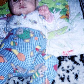 Baby wearing colorful onesie, lying on patterned blanket.