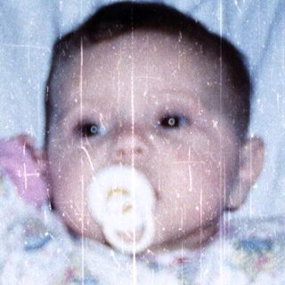 Baby wearing colorful pajamas, lying in bed with pacifier.