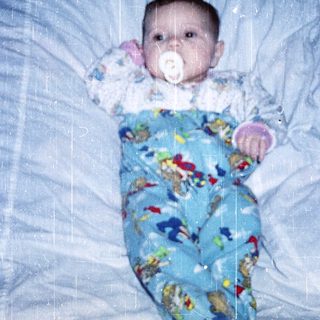 Baby wearing colorful pajamas, lying in bed with pacifier.