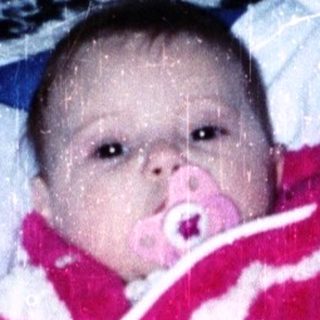 Baby in red snowsuit playing indoors with snow.
