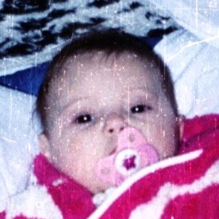Baby in red snowsuit playing indoors with snow.