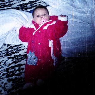 Baby in red snowsuit playing indoors with snow.