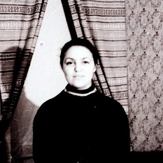 Young woman standing indoors near striped curtain.