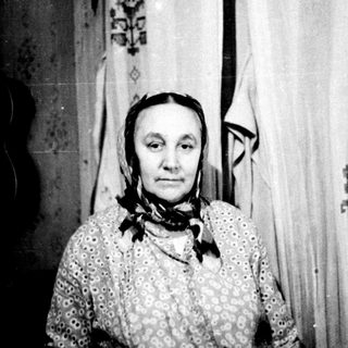 Traditional rural woman in embroidered clothing indoors.