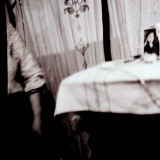 Blurred bedroom scene with bed, framed photo, and person.
