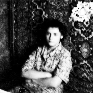 Young woman seated indoors against patterned wall.