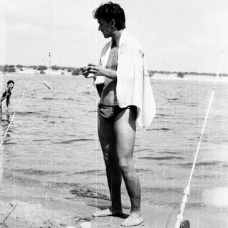 Person fishing on sandy beach near water.