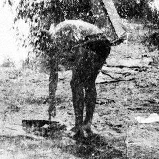 Two men carrying heavy wooden beams uphill.