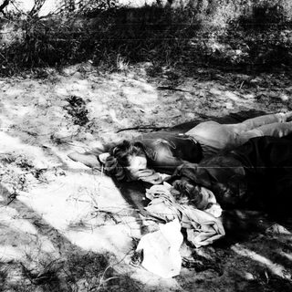 Body lying on ground near makeshift shelter.