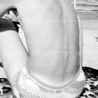 Young man sitting shirtless on beach towel.