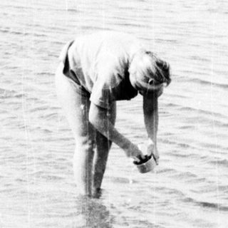 Person wading in shallow water near boats.