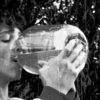 Person drinking from a bottle outdoors under trees.