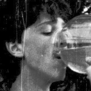 Person drinking from a bottle outdoors under trees.