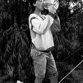 Person drinking from a bottle outdoors under trees.