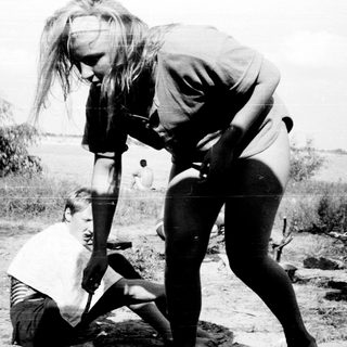 Two adults assisting a child in outdoor setting.