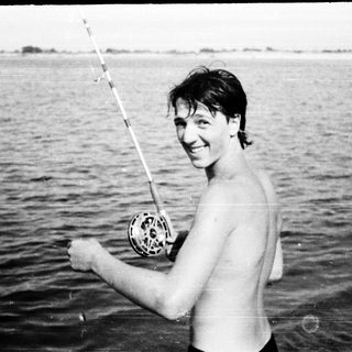 Shirtless man holding fishing rod with caught fish.