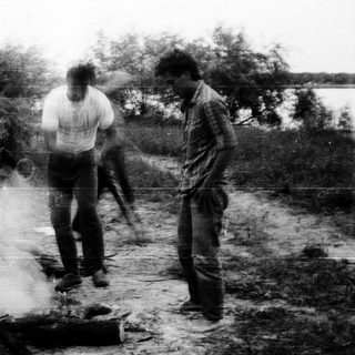 Three people camping by a small fire outdoors.